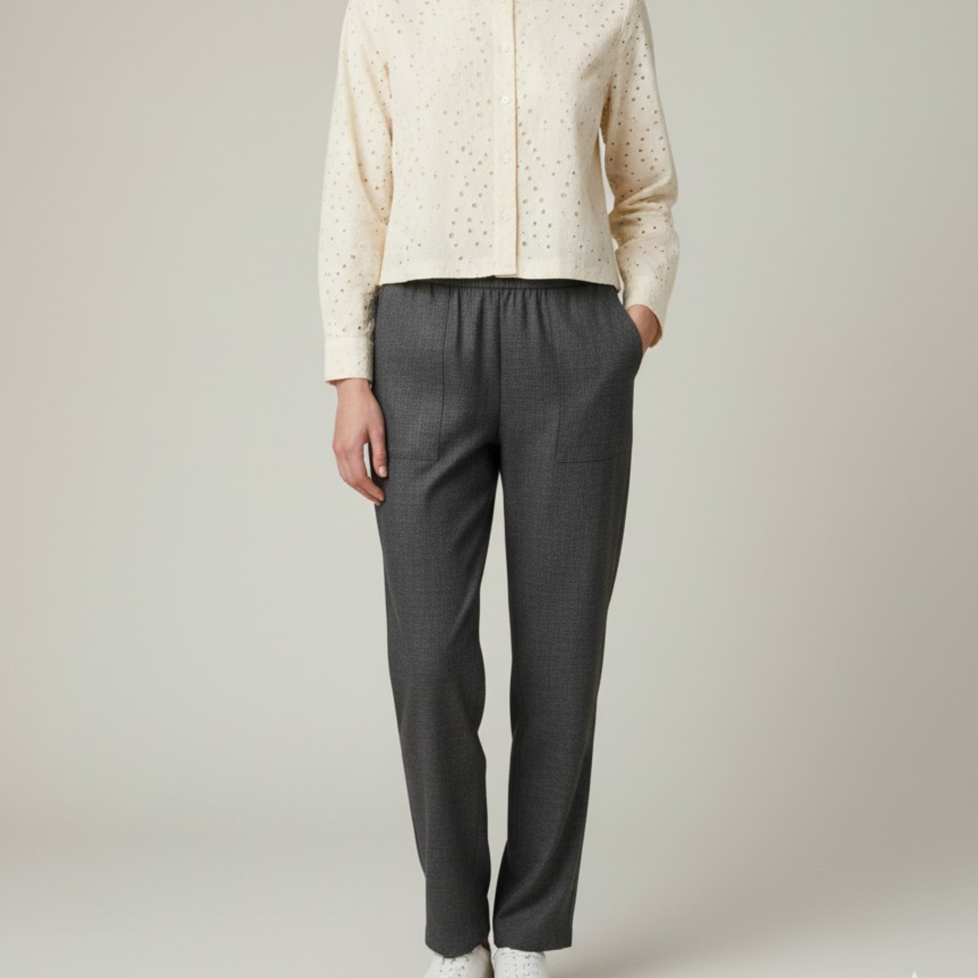 Person wearing a beige jacket and gray pants on a plain background